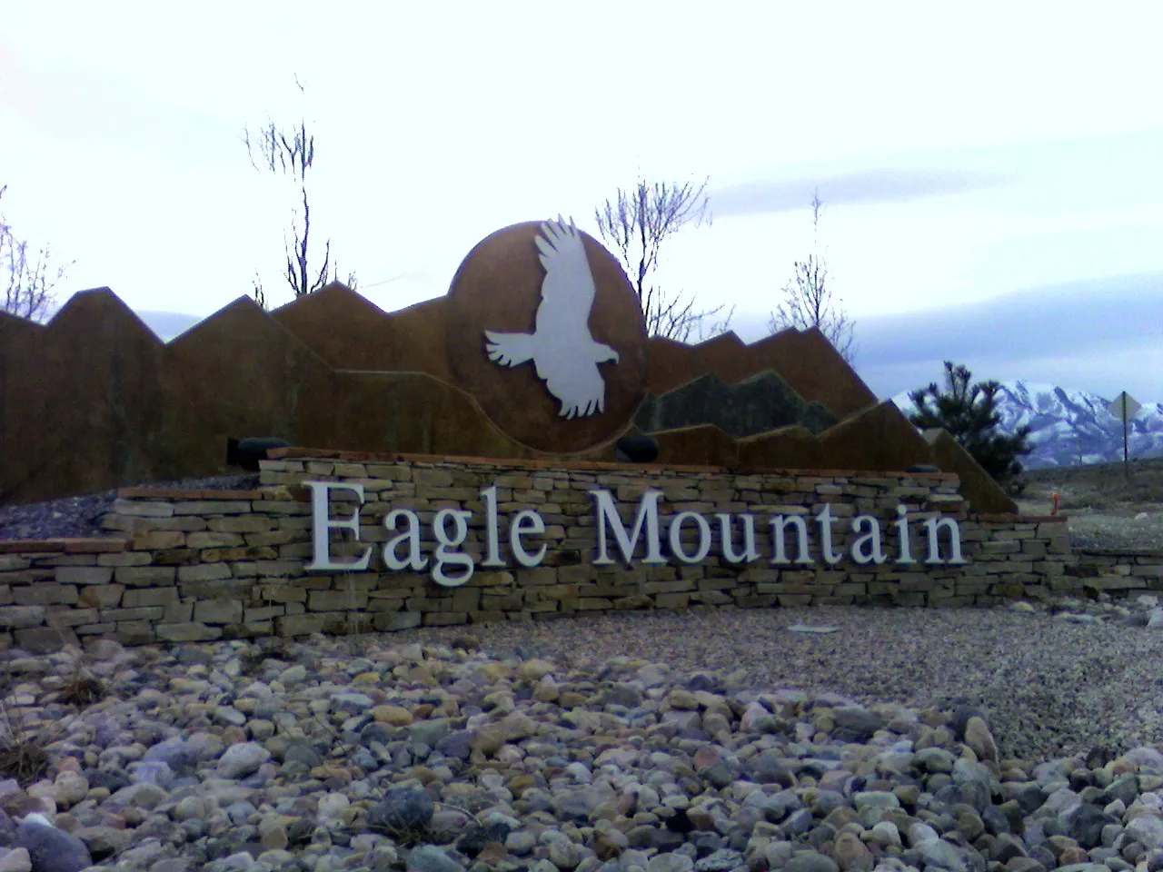 The Eagle Mountain city entrance sign, a stone wall with a silver eagle on a bronze disc and the Lake Mountains behind